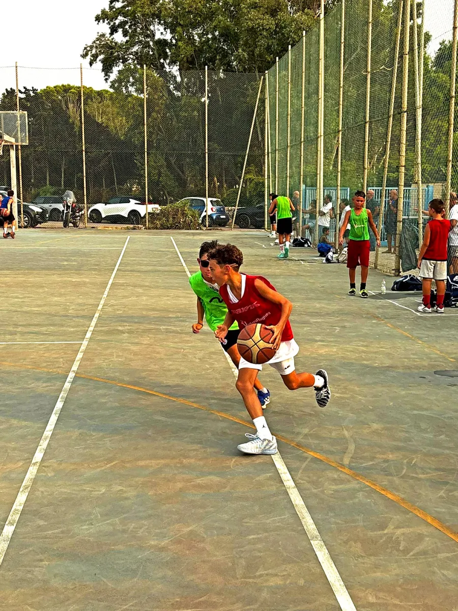 Un ragazzo in maglia rossa avanza palleggiando, inseguito da un avversario con la casacca verde.